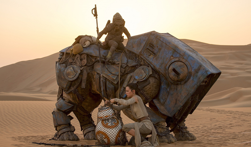 A desert scene from "Star Wars: The Force Awakens," in which the heroine Rey readies BB-8, a round android, for transport with the scavenger Teedo and his semi-mechanical Luggabeast. Photo credit: StarWars.com